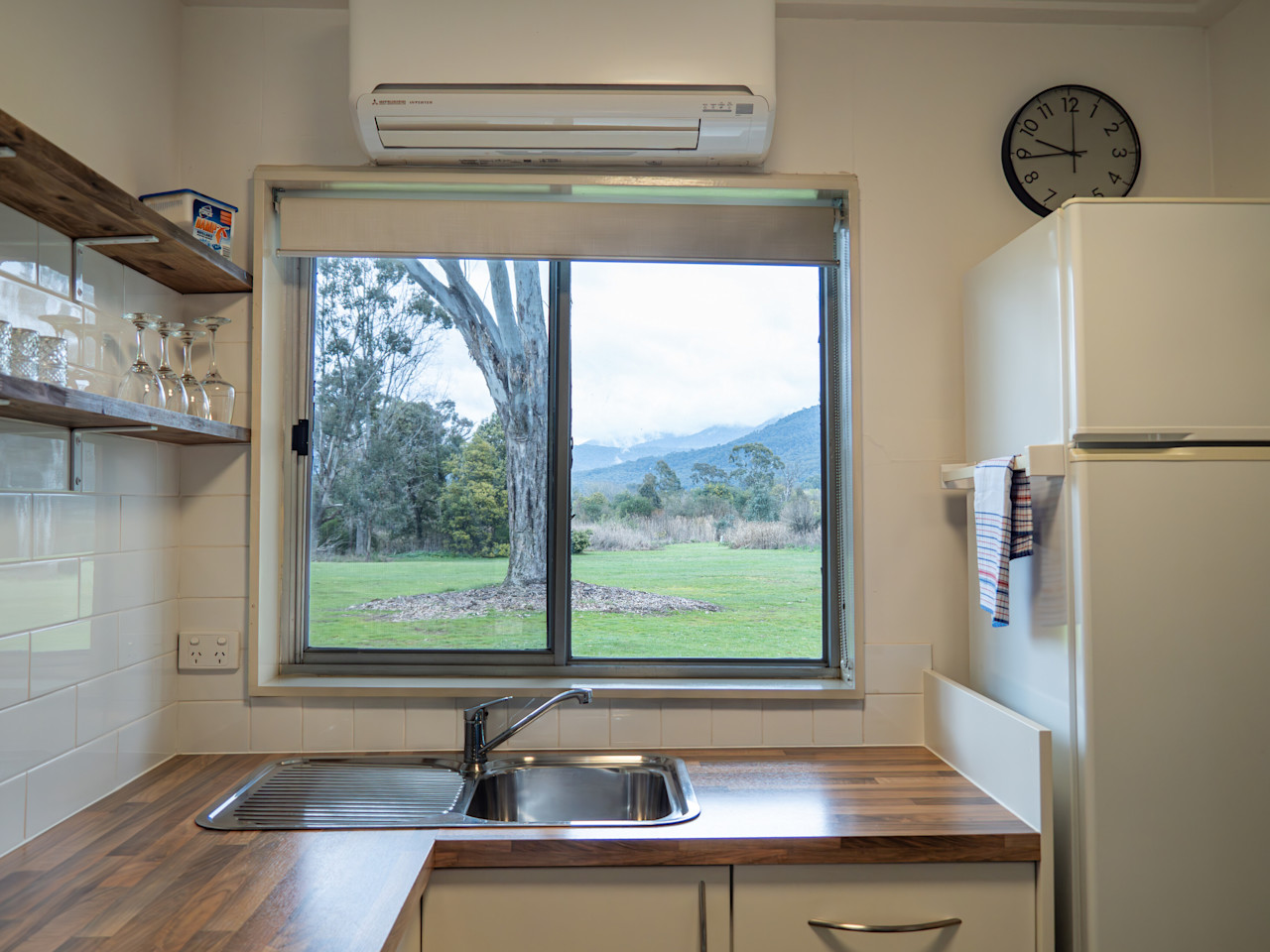 A kitchen window framing the lawn, a big gum and the ranges, above a timber benchtop and sink