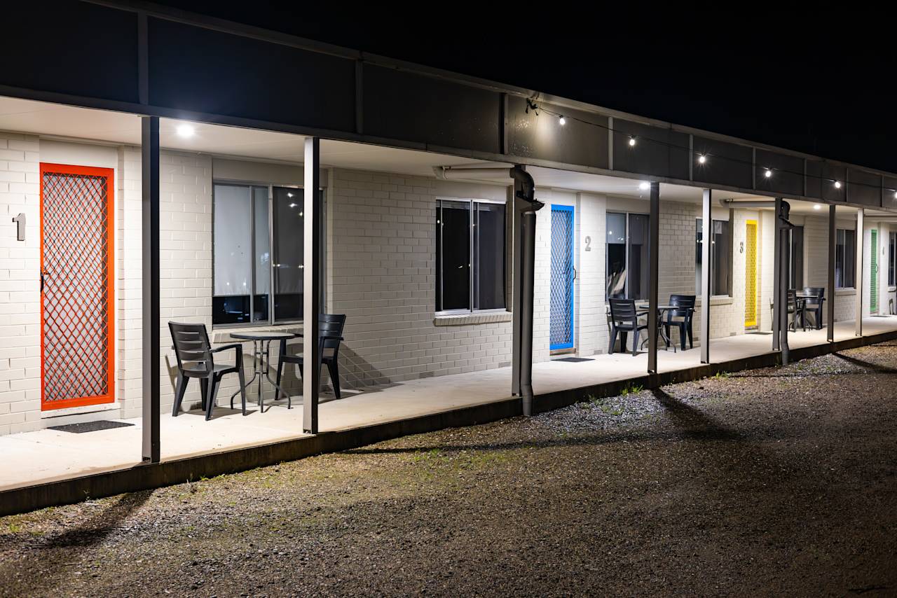 The row of units at night, each screen door a different colour, with chairs out on the veranda