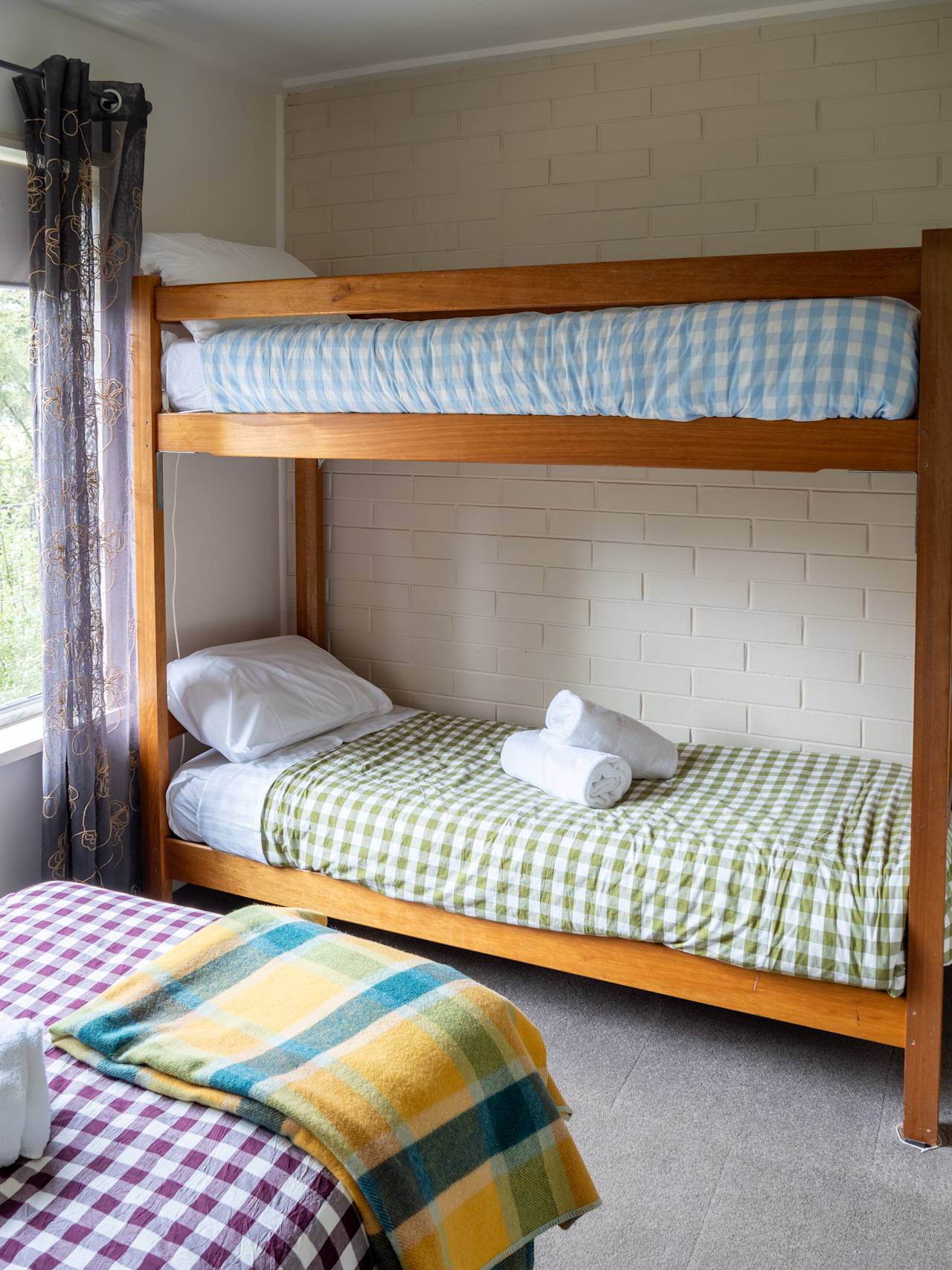 Timber bunk beds made up in gingham, beside a bed with a woollen blanket
