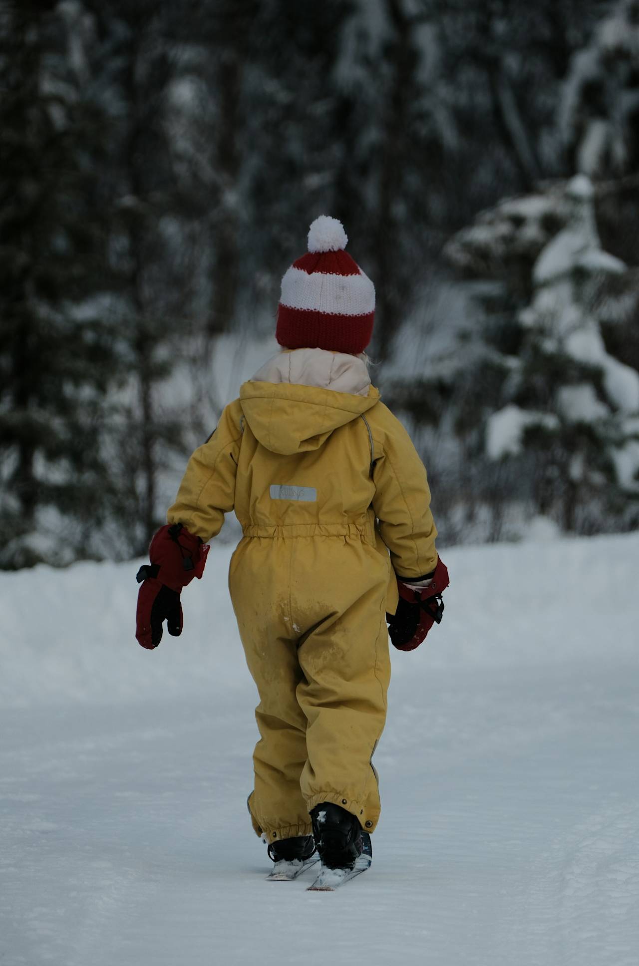 A small child in a yellow snowsuit walking through snow