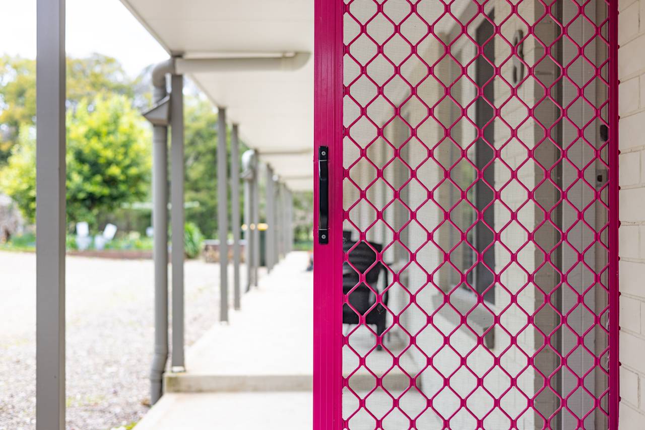 A bright pink screen door on the unit veranda, the posts running along the walkway beside it
