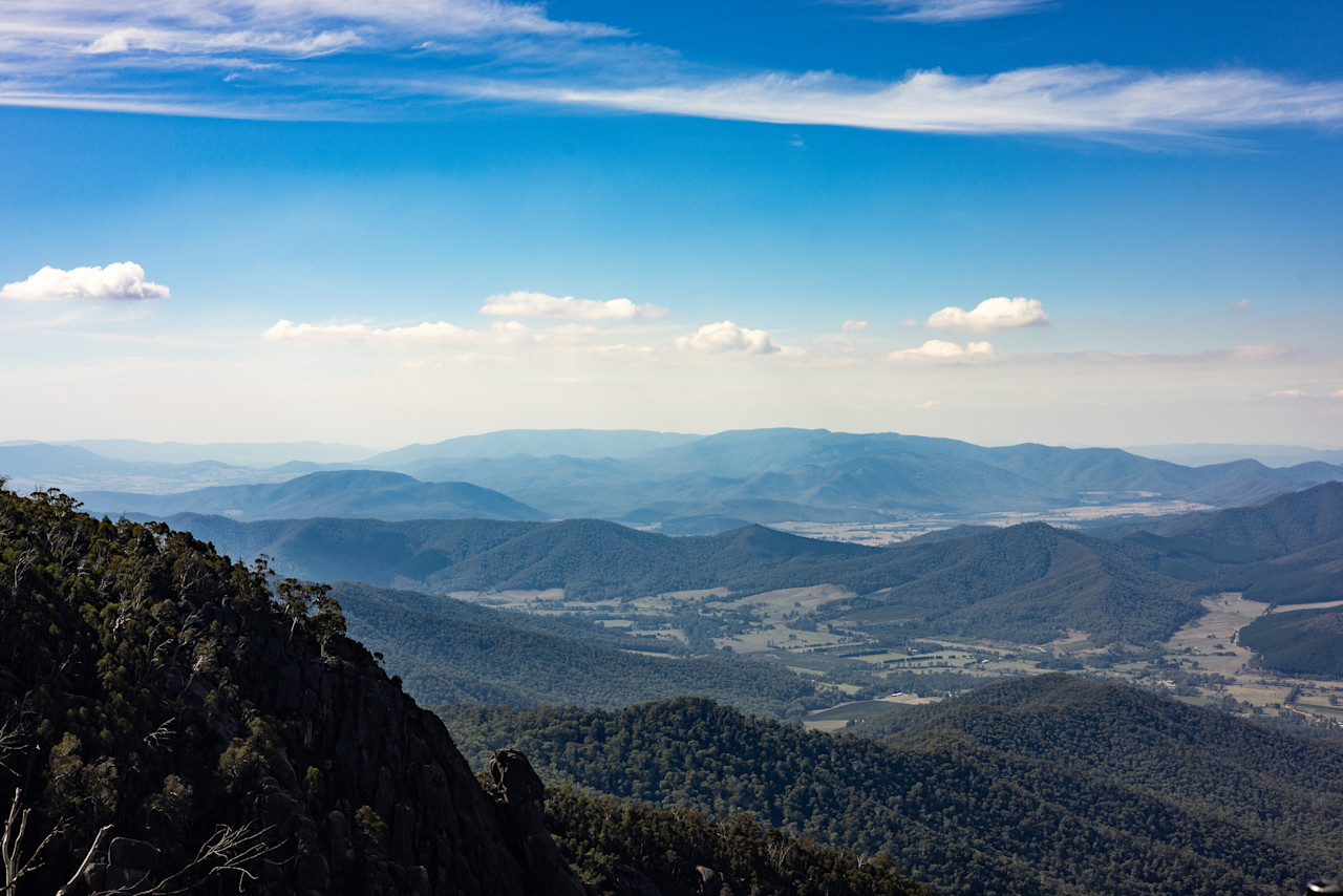 Looking out from a Mount Buffalo lookout over forested ranges and the valley below, under a blue sky