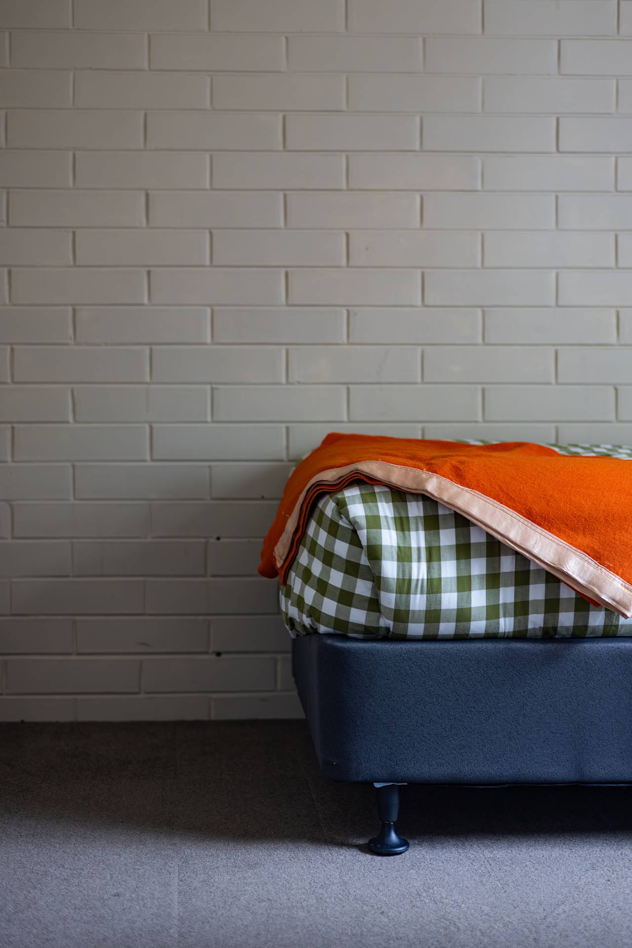A single bed with a green gingham quilt and an orange blanket folded at the foot